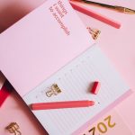 Organized workspace with pink planner, pen, and clips on pastel background.