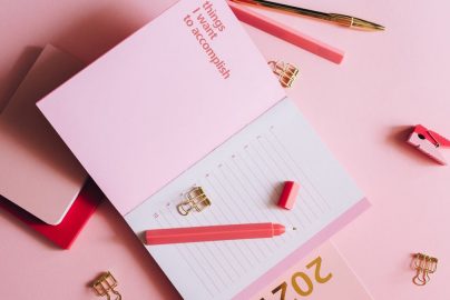 Organized workspace with pink planner, pen, and clips on pastel background.