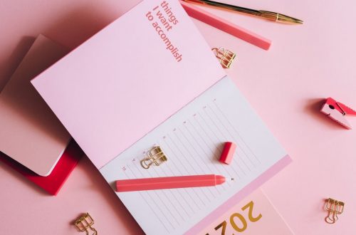 Organized workspace with pink planner, pen, and clips on pastel background.